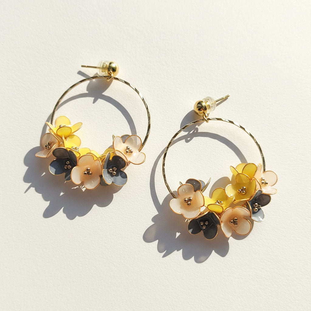 Gold hoop earrings with yellow, cream, and grey enamel flowers, handcrafted floral design on light background.