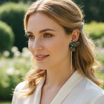 Woman wearing a decorative earring outdoors with greenery in the background