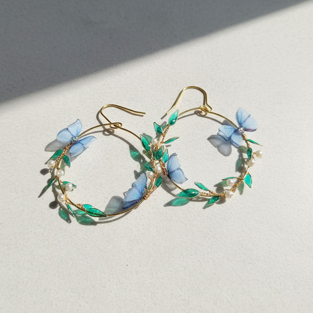 Gold hoop earrings with blue butterfly and green leaf details on a light background