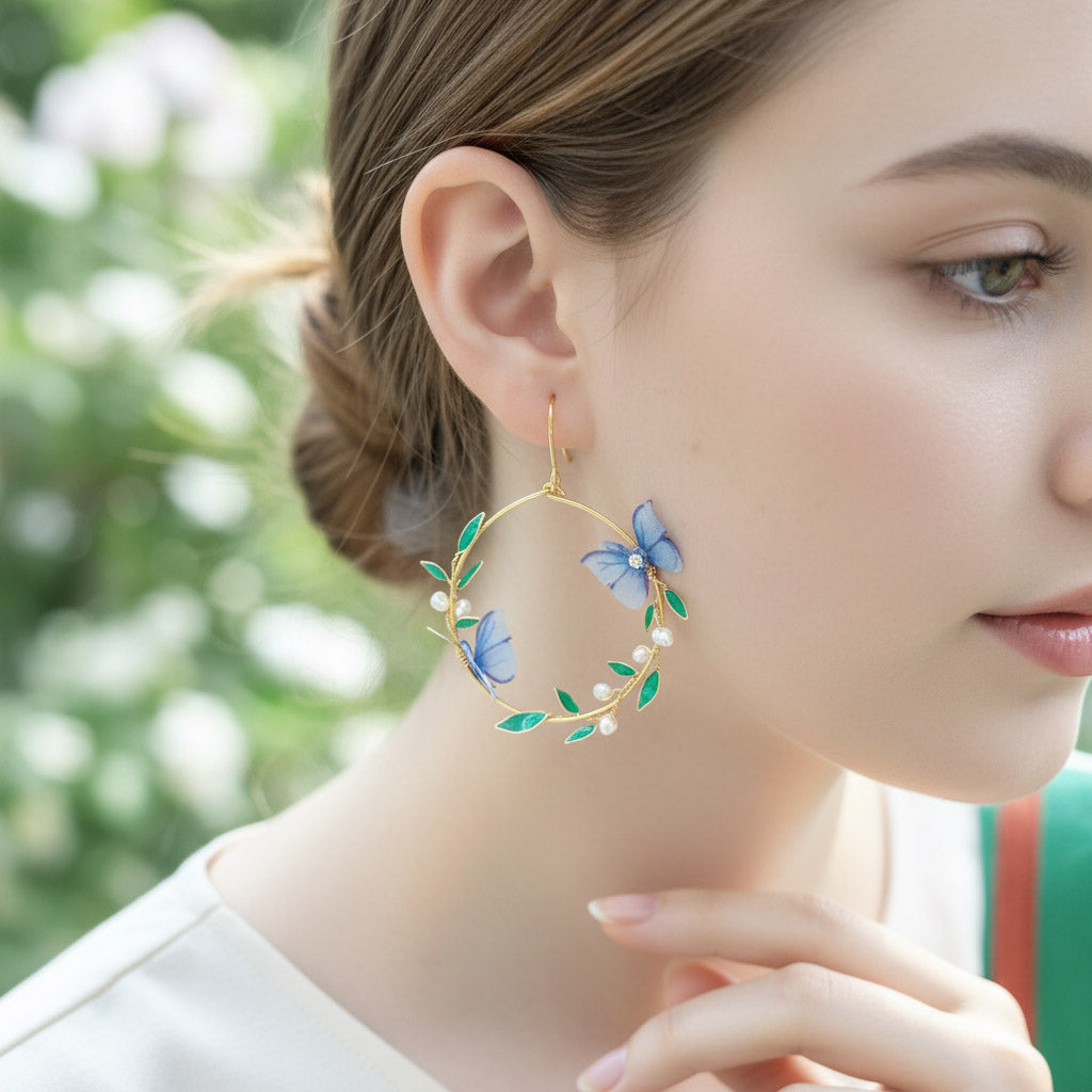 Close-up of a woman wearing gold hoop earrings with blue butterfly and green leaf designs.