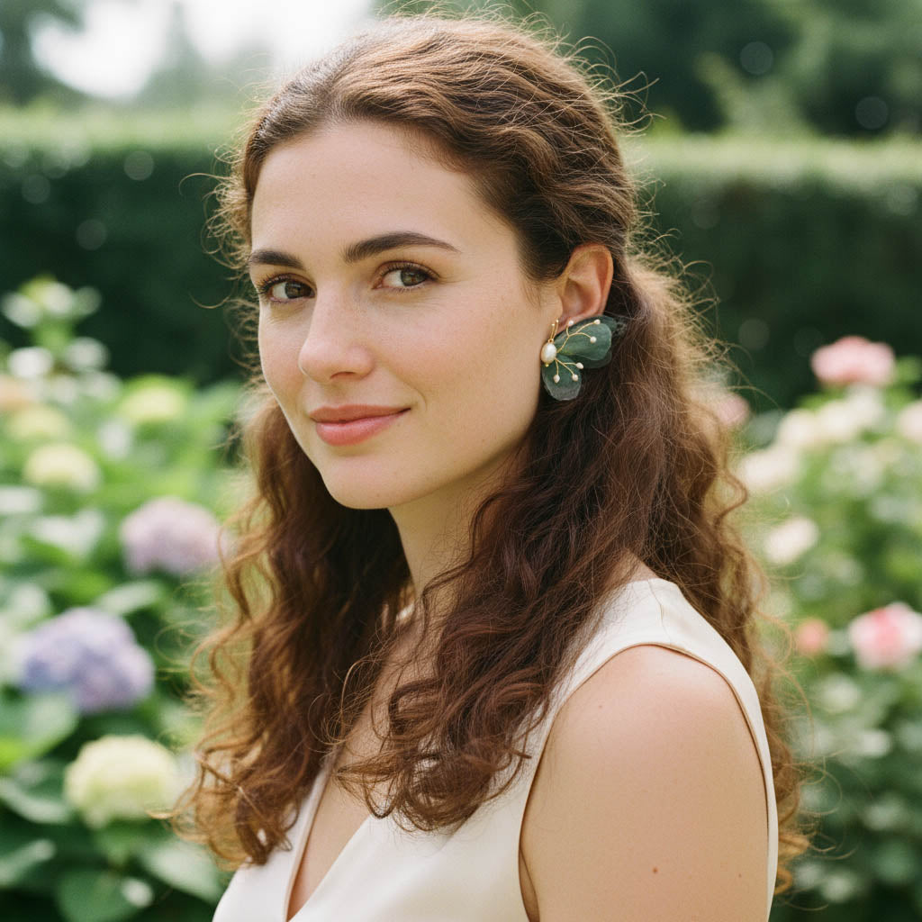 Woman wearing elegant green butterfly earrings with gold accents in a garden setting.