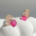 Pair of pink and gold earrings on a white surface with a gray background