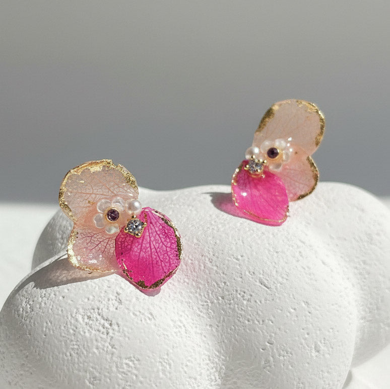 Pair of pink and gold earrings on a white surface with a gray background