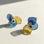 Pair of earrings with blue and yellow leaf designs on a light background