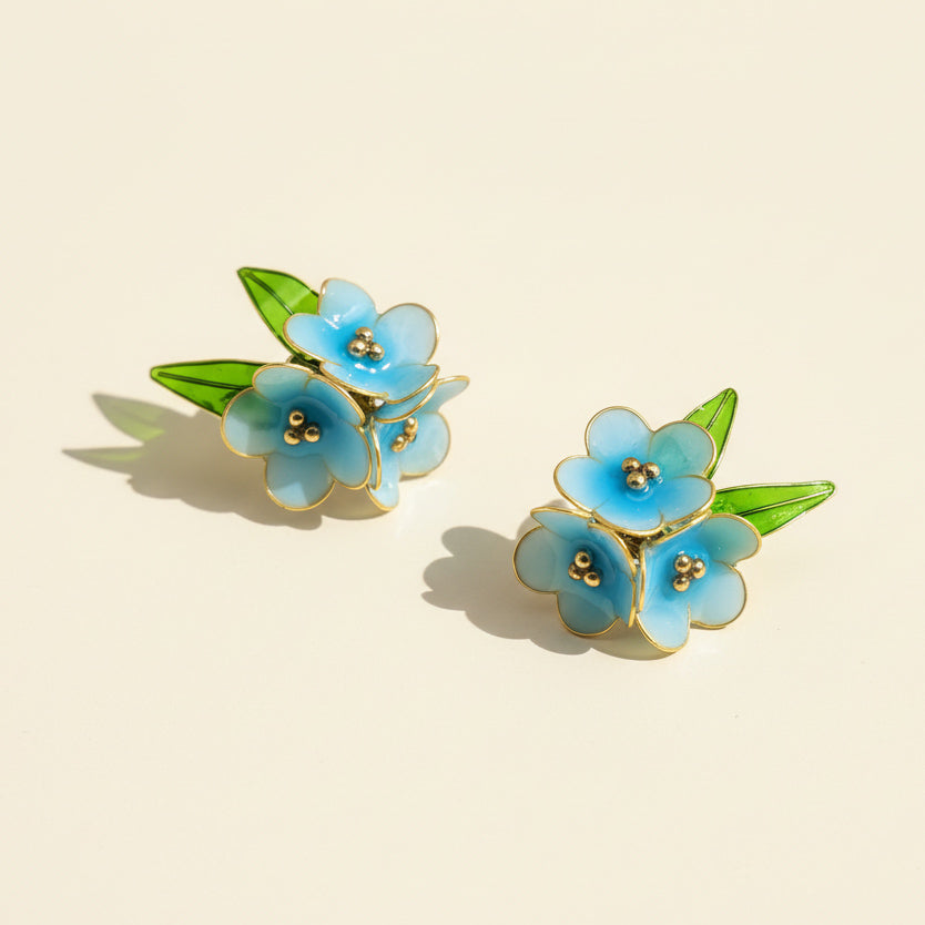 Floral earrings with blue flowers and green leaves on a beige background