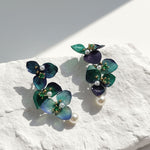 Pair of floral earrings with green and blue hues on a textured white surface