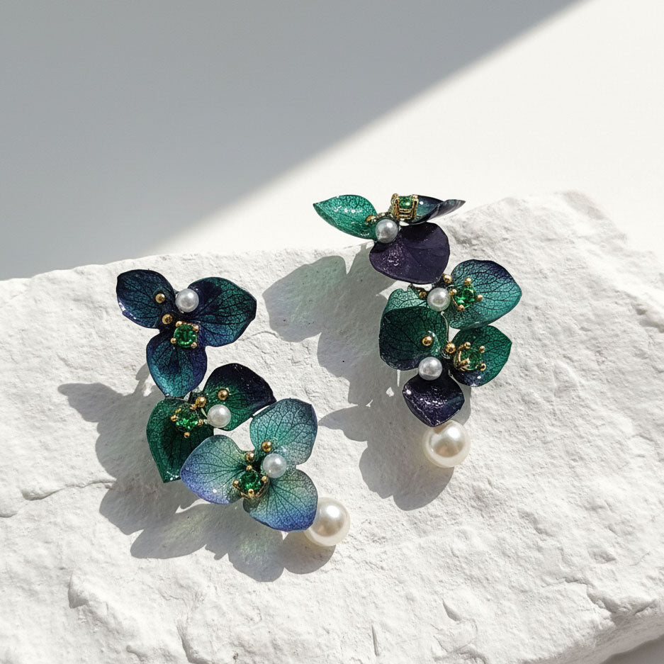 Pair of floral earrings with green and blue hues on a textured white surface