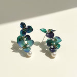 Pair of floral earrings with green and blue leaves on a beige background