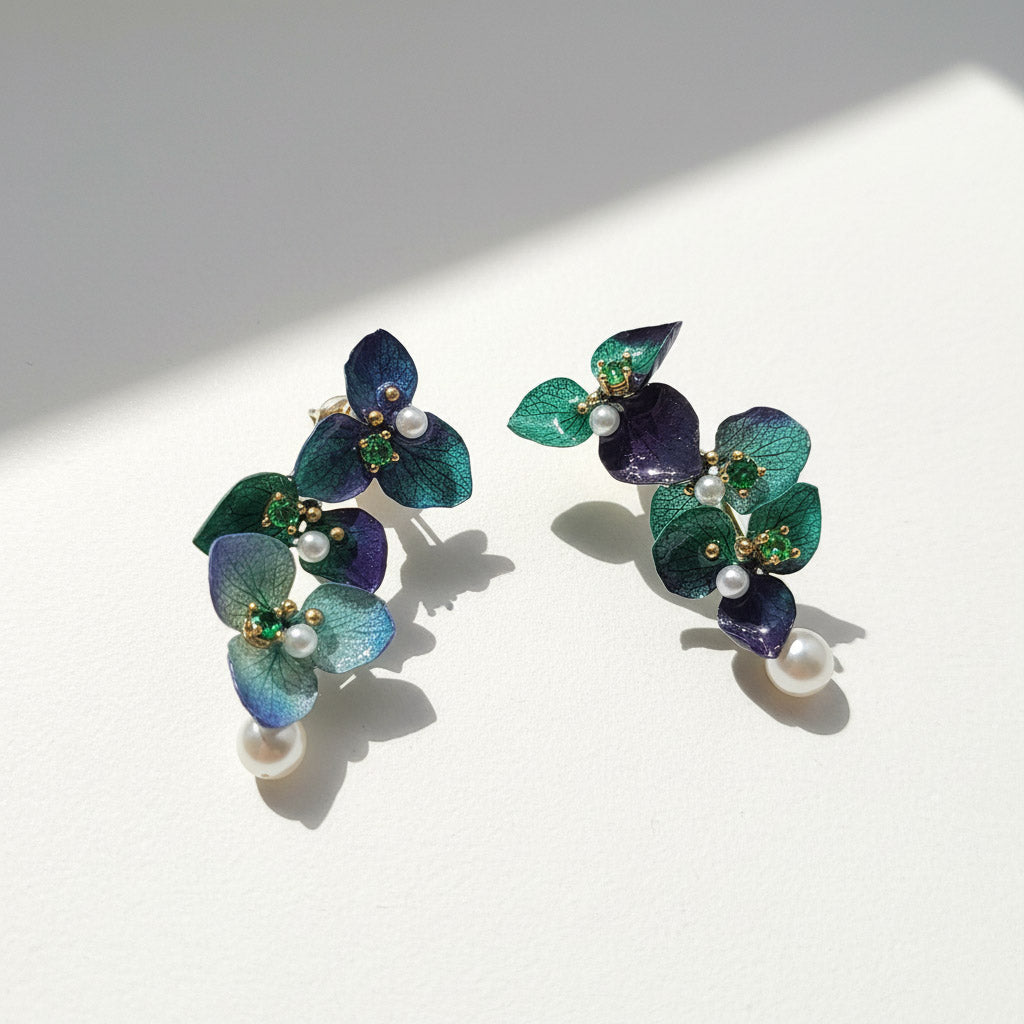 Pair of floral earrings with green and blue leaves on a white background