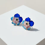 Pair of floral earrings with blue, pink, and white colors on a light background