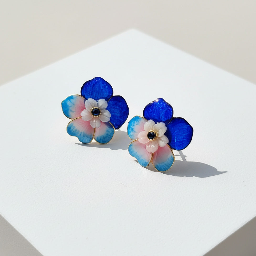 Pair of floral earrings with blue, pink, and white colors on a light background