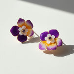 Flower-shaped earrings with purple, orange, and white colors on a light background