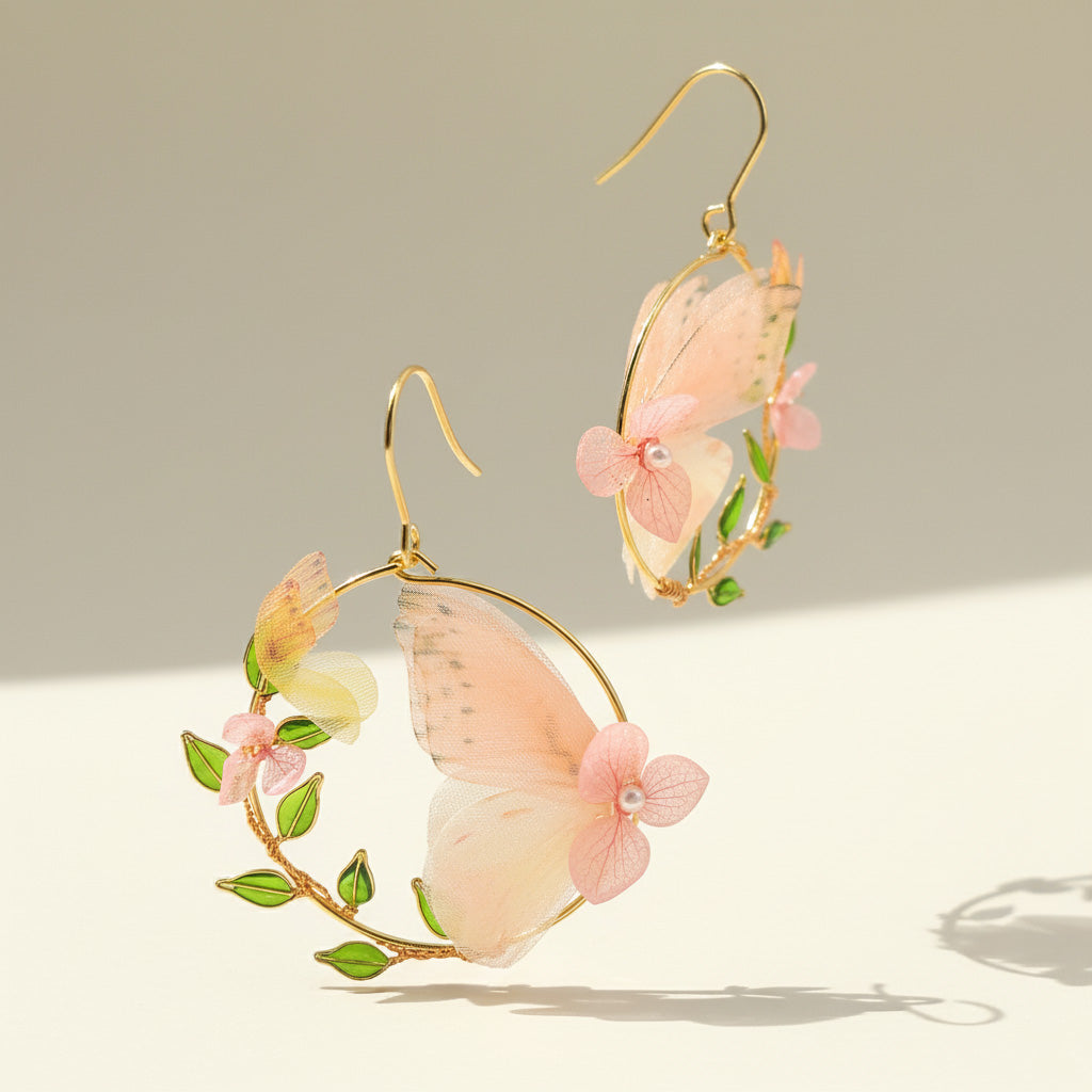 Butterfly-shaped earrings with pink wings and green leaves on a neutral background