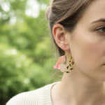 Close-up of a woman wearing floral earrings with a blurred green background