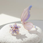 Butterfly and flower-shaped earrings with purple and gold accents on a light surface.