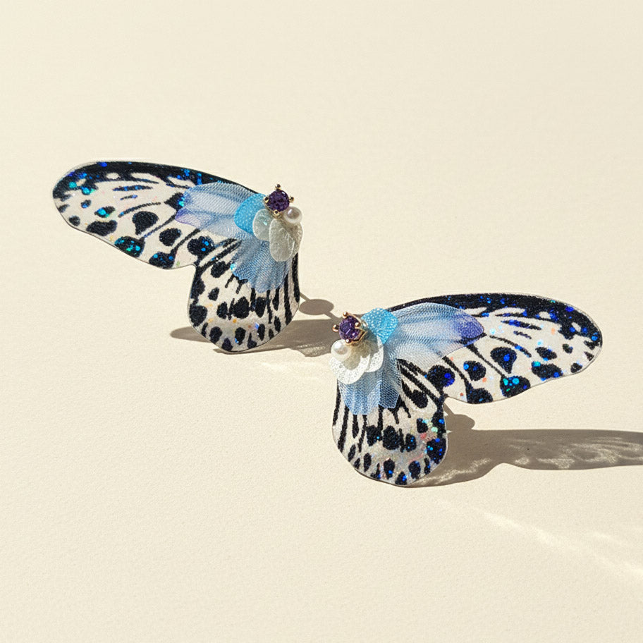 Butterfly-shaped earrings with blue and black patterns on a beige background