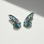 Delicate green and black butterfly wing earrings with pearl and gemstone details on a white background.