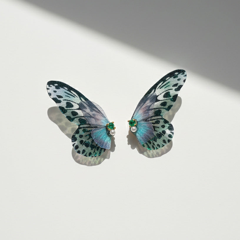 Delicate green and black butterfly wing earrings with pearl and gemstone details on a white background.