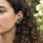 Woman wearing green butterfly wing earrings with pearl and gemstone accents in natural outdoor light.