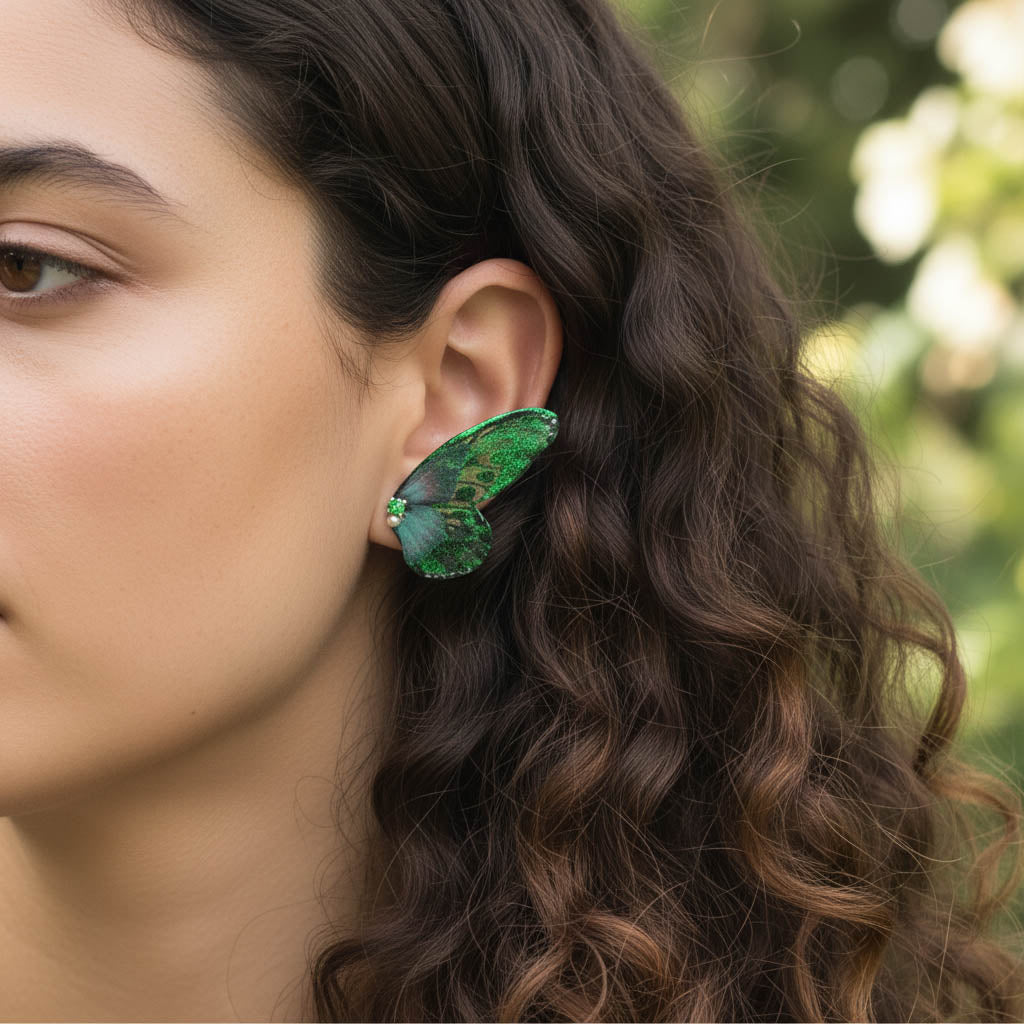 Woman wearing green butterfly wing earrings with pearl and gemstone accents in natural outdoor light.