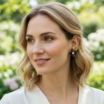 Woman with blonde hair and floral earrings against a blurred green and white background