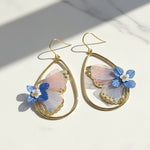 Gold earrings with butterfly-shaped flowers on a light background