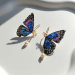 Butterfly-shaped earrings with gold hooks and pearl drops on a white fabric background