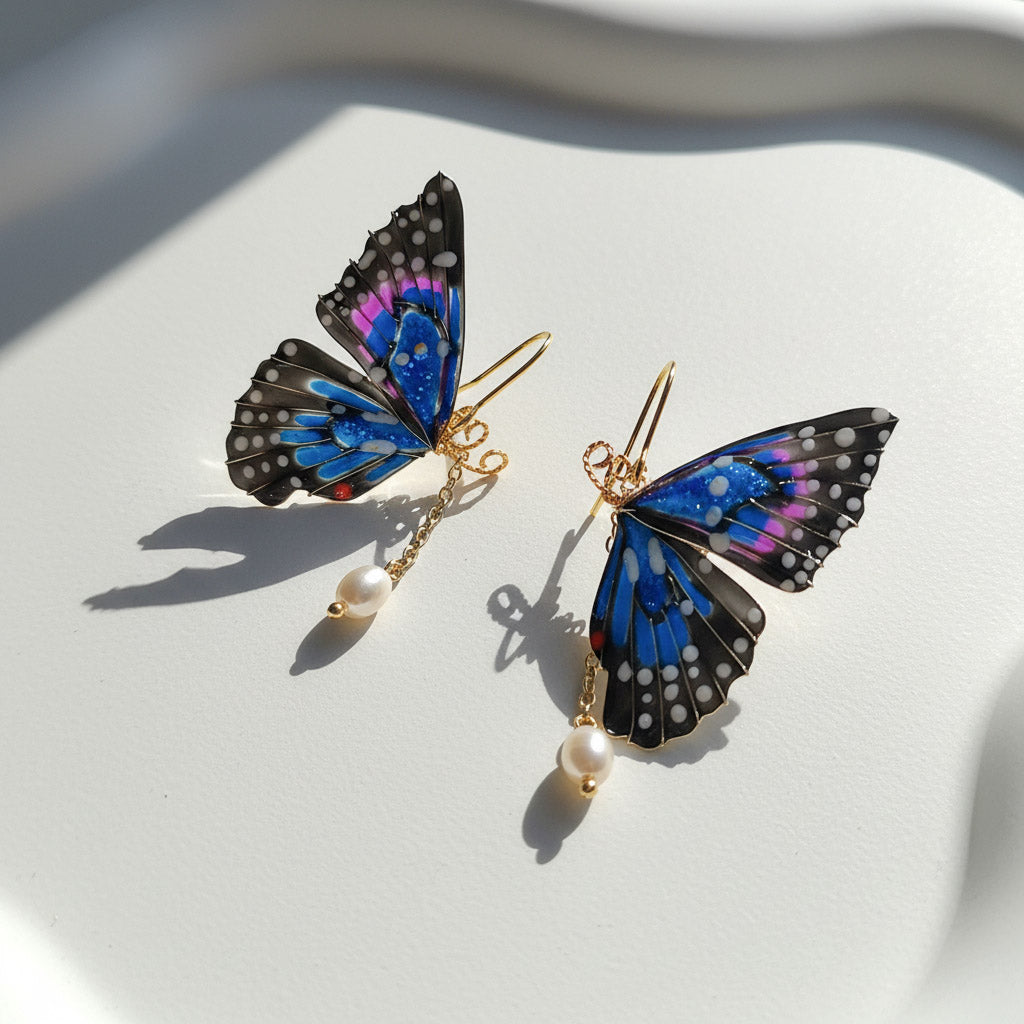 Butterfly-shaped earrings with gold hooks and pearl drops on a white fabric background