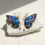 Butterfly-shaped earrings with pearl drops on a white stone surface