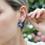 Person wearing blue floral earrings with a blurred natural background