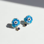 Blue flower-shaped earrings with white centers and small blue stones on a light background