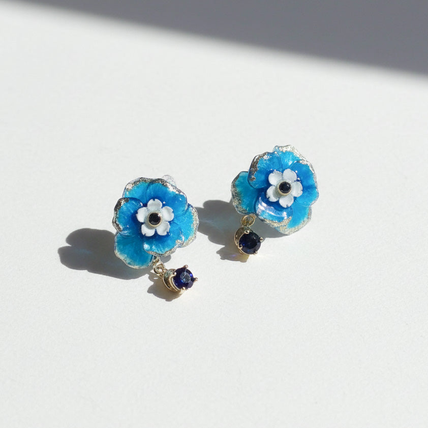 Blue flower-shaped earrings with white centers and small blue stones on a light background