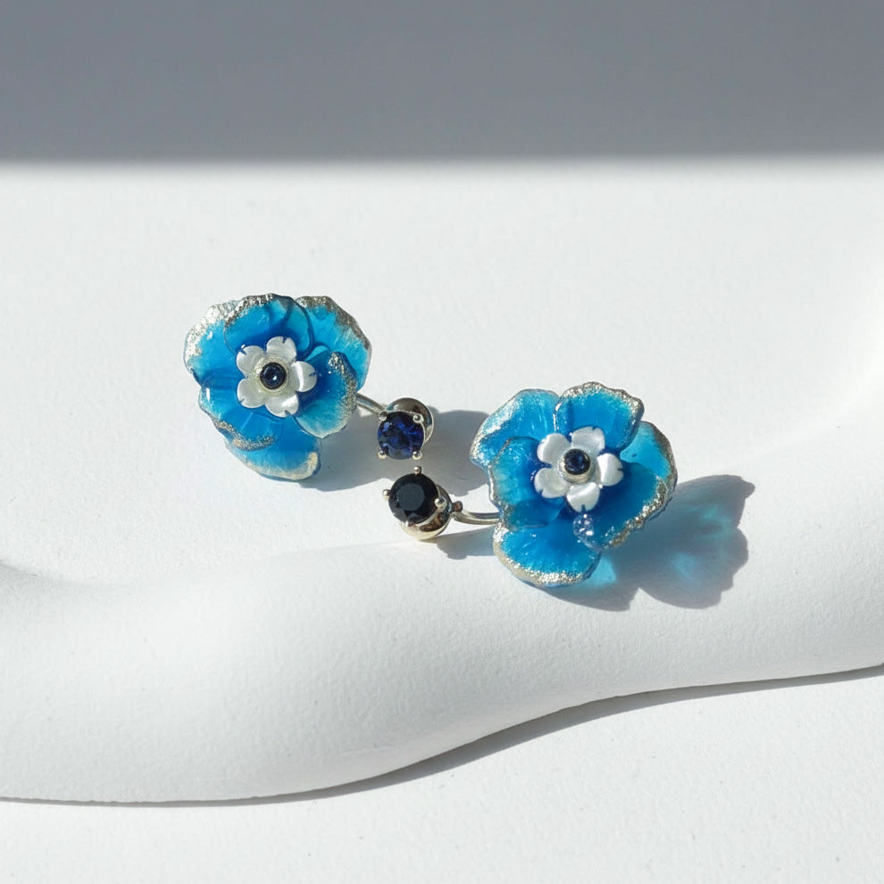 Pair of blue flower earrings with black centers on a white surface