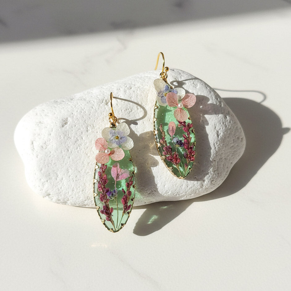 Pressed flower resin teardrop earrings with pink and purple blooms on white background
