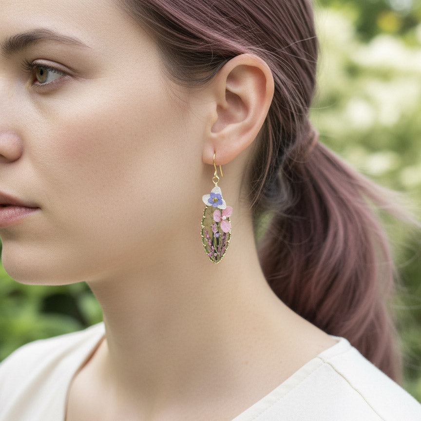 Model wearing pressed flower teardrop resin earrings with pastel blooms outdoors.