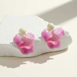 Pink flower-shaped earrings on a white stone surface