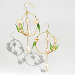 Gold hoop earrings with pearl and leaf details on a light gray background