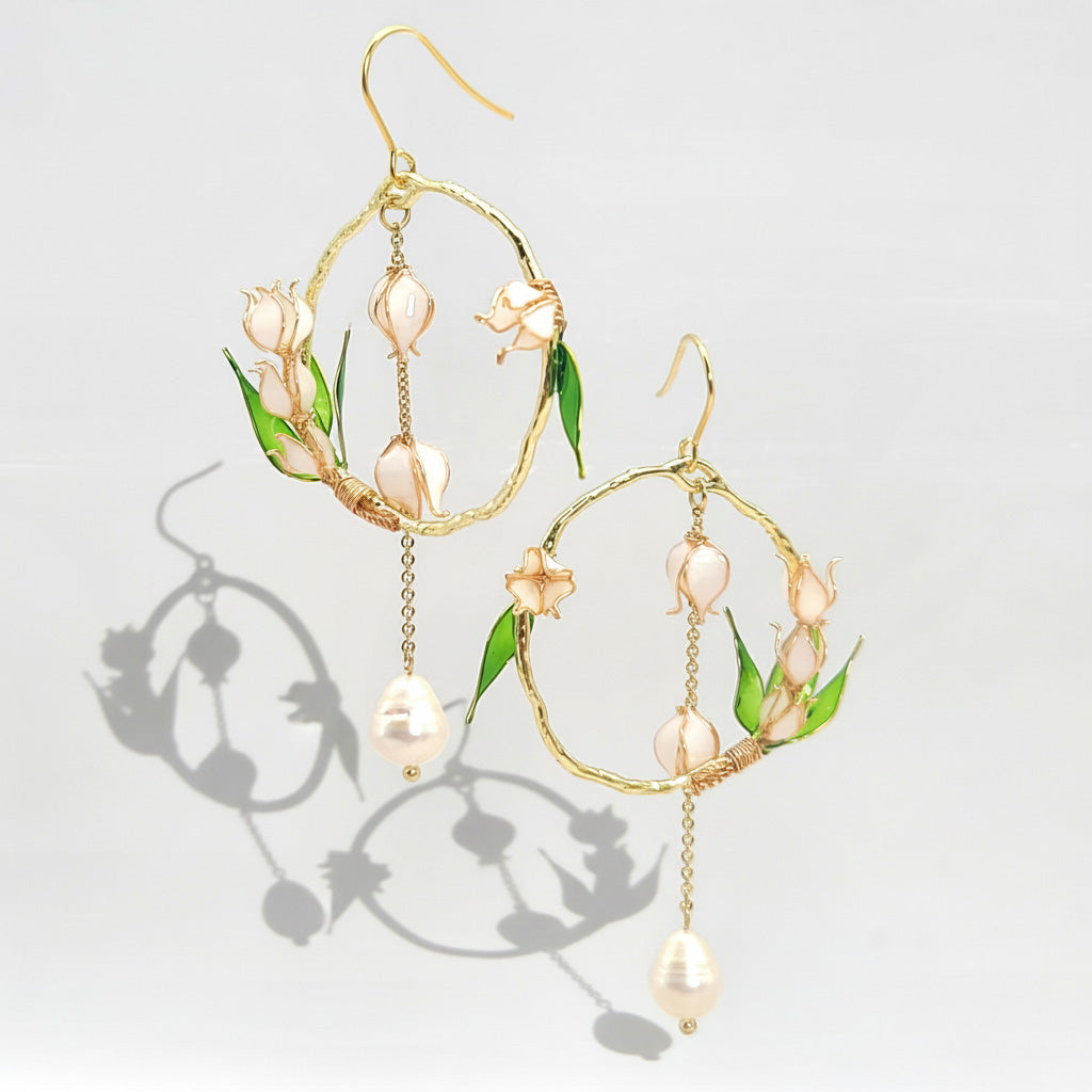 Gold hoop earrings with pearl and leaf details on a light gray background