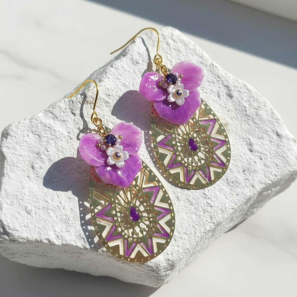 Purple floral earrings with gold geometric designs on a textured white surface