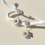 Pair of floral earrings with colorful stones on a white branch against a beige background