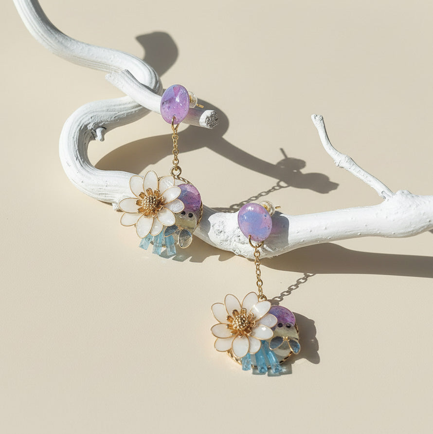 Pair of floral earrings with colorful stones on a white branch against a beige background