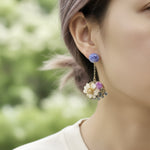 Close-up of a person wearing floral earrings with a blurred green background