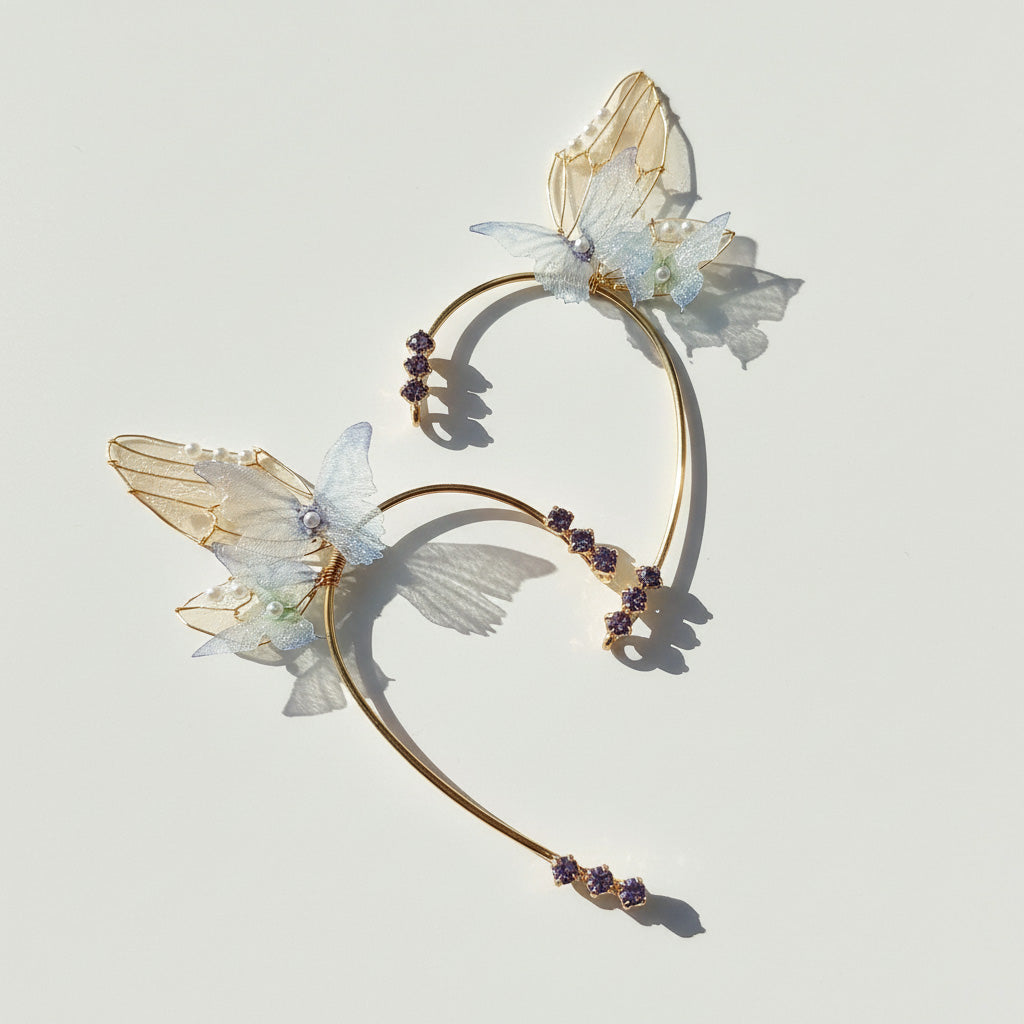 Gold butterfly ear cuffs with translucent wings, pearl accents, and purple crystals on light background.
