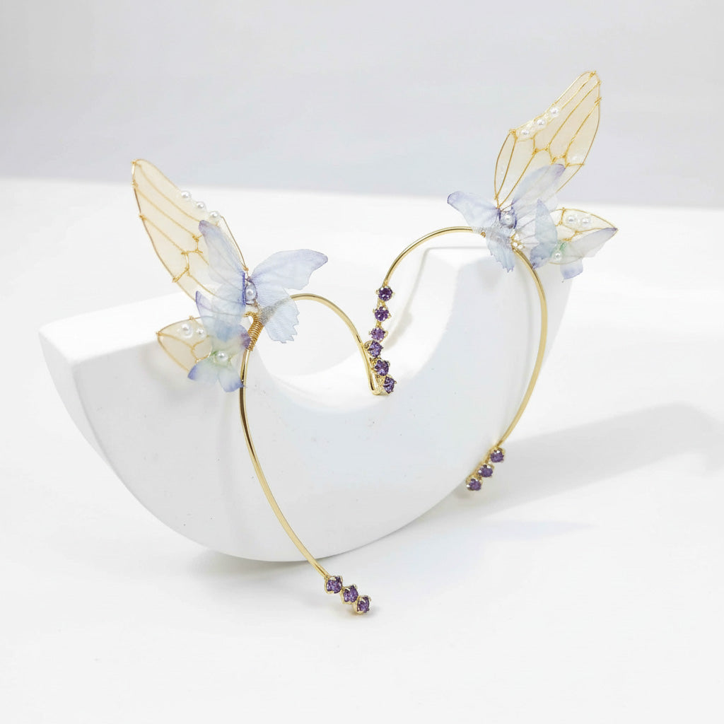 Delicate gold butterfly ear cuffs with translucent blue wings and purple crystal accents displayed on white stand.