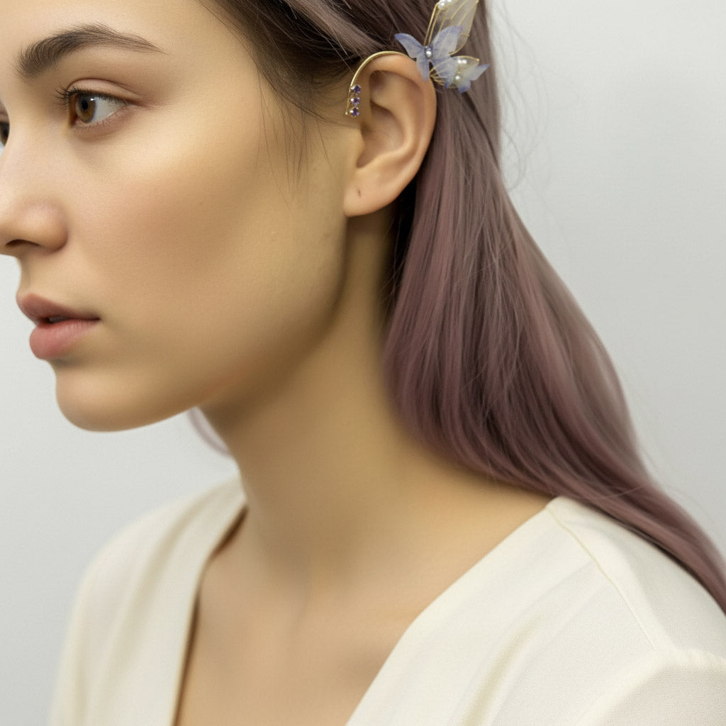 Model wearing gold butterfly ear cuff with translucent wings and purple crystals, styled with soft lavender hair.