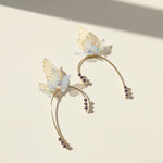 Gold ear cuffs with delicate blue flowers, butterfly wings, and purple crystal details in ethereal design.
