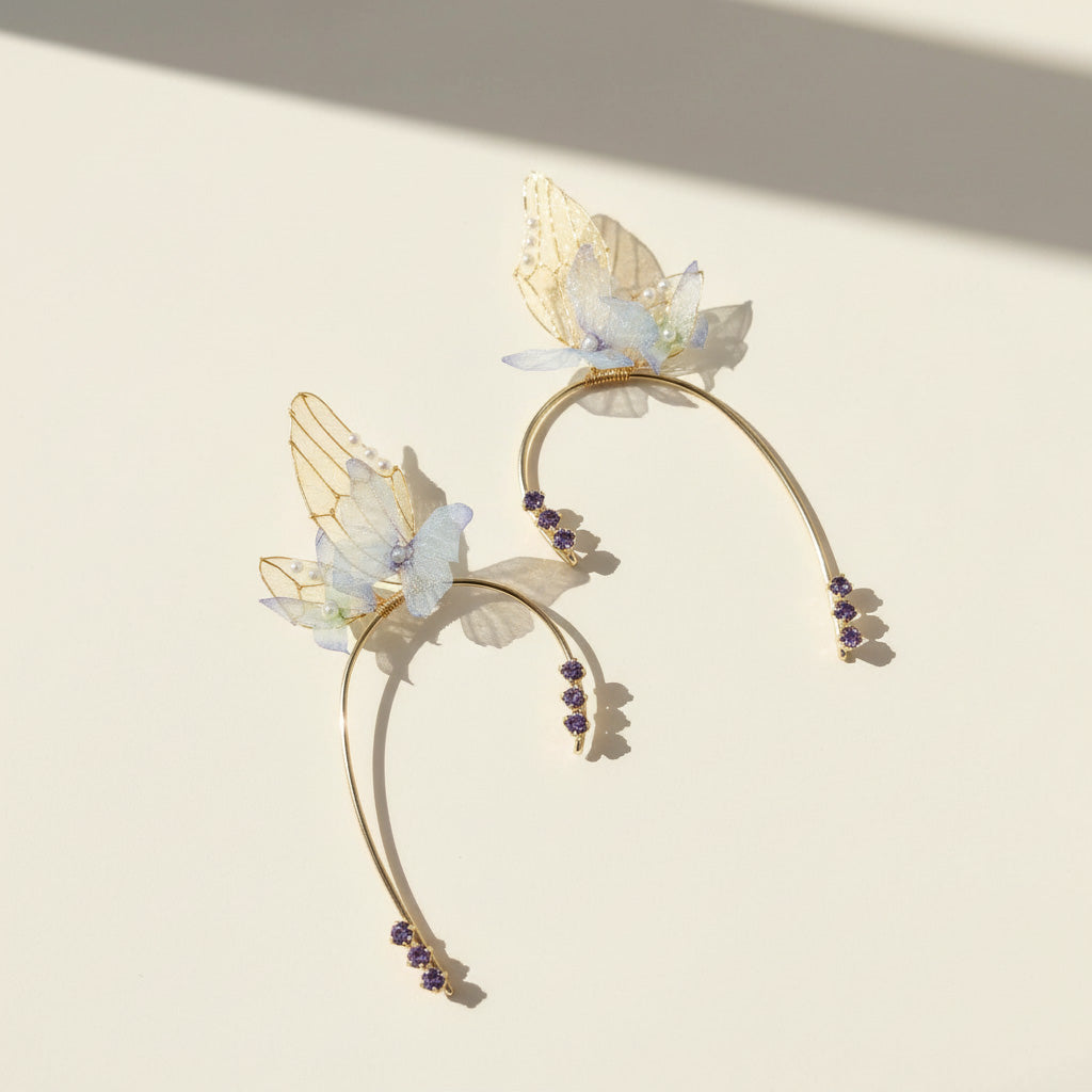 Gold ear cuffs with delicate blue flowers, butterfly wings, and purple crystal details in ethereal design.