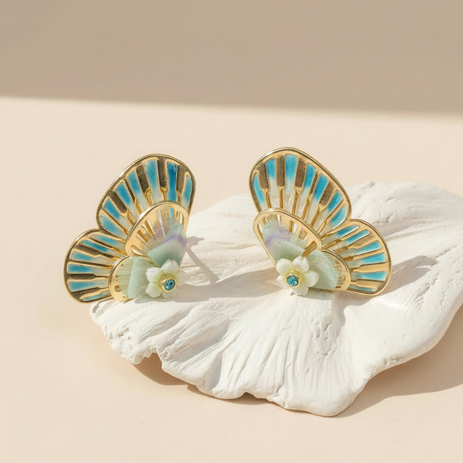 Pair of gold and turquoise earrings on a white shell against a beige background