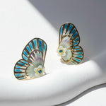 Butterfly-shaped earrings with blue and gold details on a white stand.