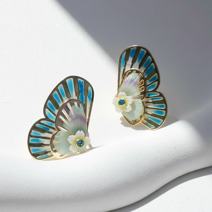 Butterfly-shaped earrings with blue and gold details on a white stand.